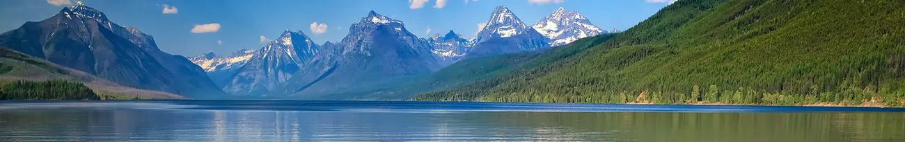 Panoramic view of Lake McDonald with crystal-clear turquoise waters, surrounding pine forests and snow-capped mountains of Glacier National Park