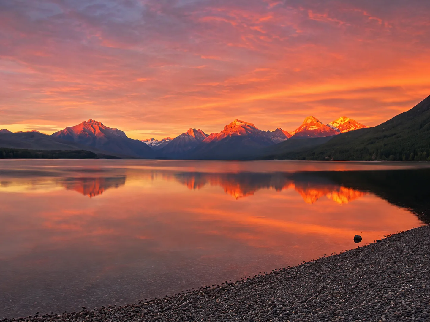 Mountain peaks glowing orange with alpenglow above Lake McDonald after sunset