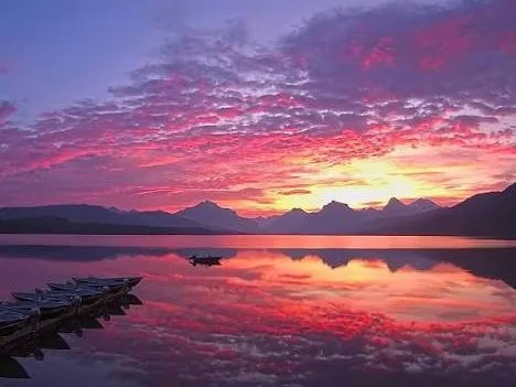 Canoes moored at the Apgar dock on Lake McDonald under a vivid pink sunset sky