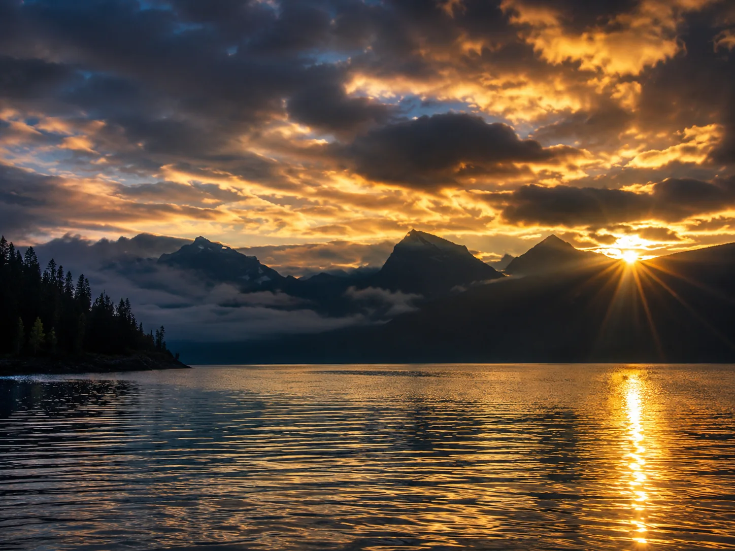 Dramatic storm clouds breaking at sunset over Lake McDonald with sunburst near the mountains