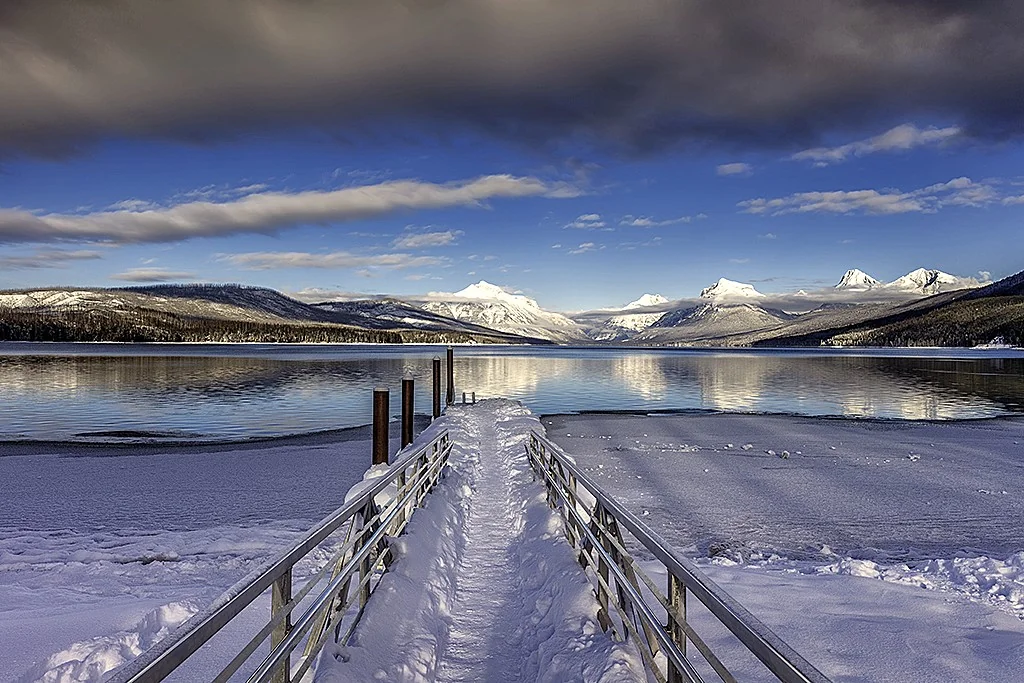 Lake McDonald in winter with snow-covered peaks reflected in the partially frozen lake surface